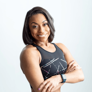 Headshot of Ashley Nicole. Brown-skinned female fitness professional in purple and black workout attire with shoulder length straight natural hair with a Apple watch on.